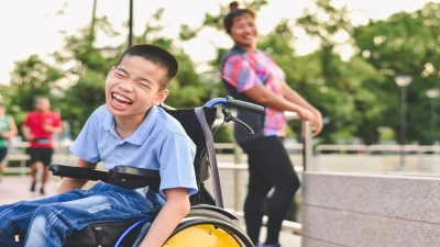 child in wheelchair with person standing behind