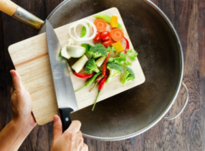 hand holding knife, sliding chopped vegetables off of cutting board into pan