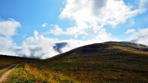 photo of grassy hill with cloudy blue sky