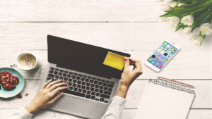 photo of a laptop with a person putting a sticky note on the screen and a phone and tablet