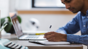 photo of man sitting at a desk working with a pen, paper and computer
