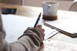 person takes notes on wood table with coffee mug