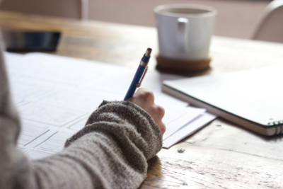 person takes notes on wood table with coffee mug