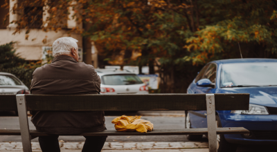 elder gentleman sits on bench looking at street scene